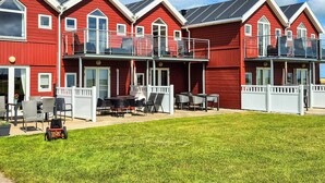 A row of red buildings with balconies, a grassy lawn, and outdoor furniture. - 6 Person Holiday Home in Hadsund (Hadsund)
