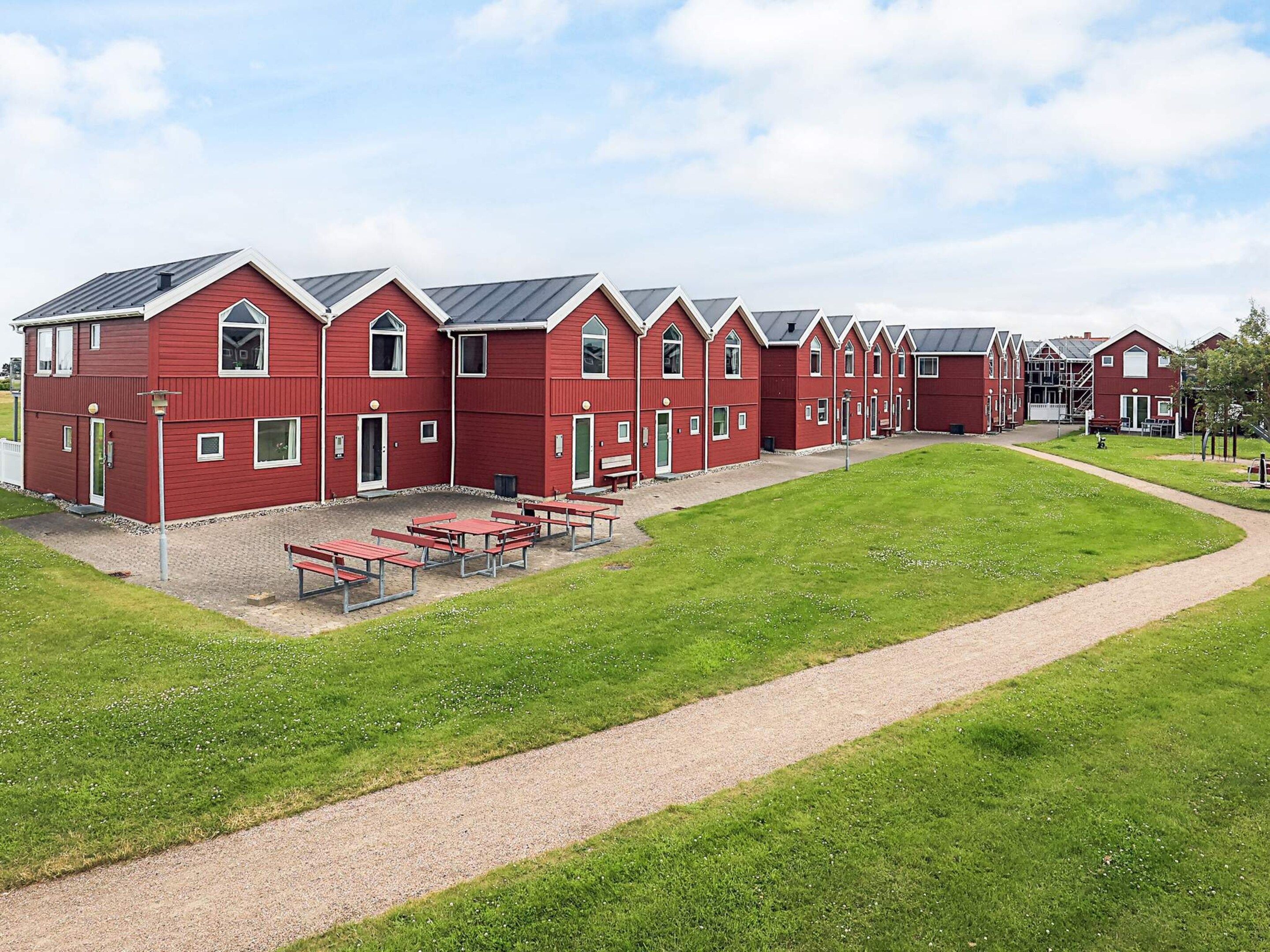 A row of red buildings with a gravel path leading to picnic tables.