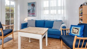 Ein Wohnzimmer mit einem blauen Sofa, Holzstühlen, einem Couchtisch und einem Bild an der Wand.