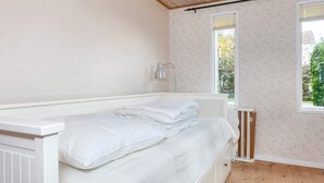 Ein kleines, ordentliches Schlafzimmer mit einem Einzelbett, einem Heizkörper und einem Fenster mit Blick auf Grünflächen.