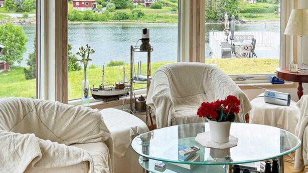 A room with a large window overlooking a lake, furnished with white chairs and a glass table. - 4 Star Holiday Home in Vaddo (Väddö)