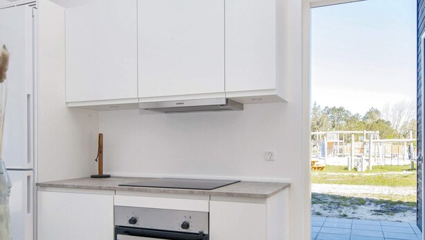 A kitchen with white cabinets, a built-in oven, and a view of a playground outside. - 5 Star Holiday Home in Romo (Rømø)