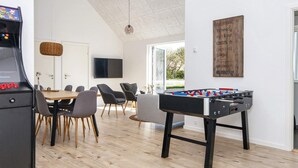 A modern living room with a foosball table, a gaming console, a dining area with a table and chairs, and a mounted TV. - 5 Star Holiday Home in Romo (Rømø)