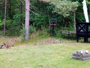 A grassy area with a wooden bench, a black metal structure, and a birdhouse. - 6 Person Holiday Home in Hadsund (Hadsund)
