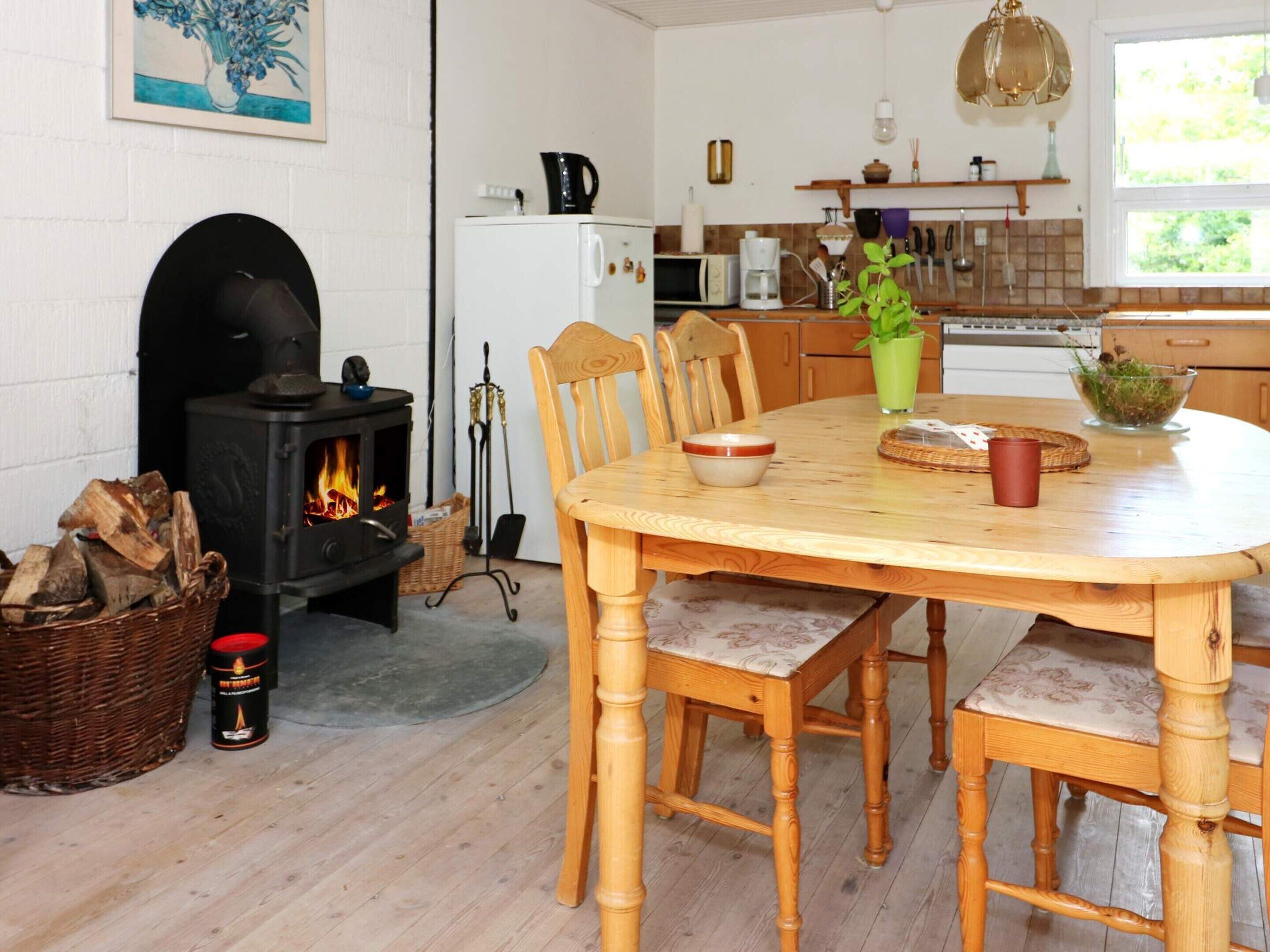 A cozy dining area with a round wooden table, chairs, a fireplace, and a kitchen in the background.