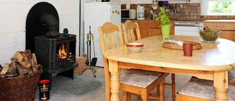 A cozy dining area with a round wooden table, chairs, a fireplace, and a kitchen in the background.