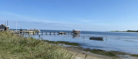 A coastal scene with a pier extending into calm waters, a small boat docked at the end, and a grassy area in the foreground.