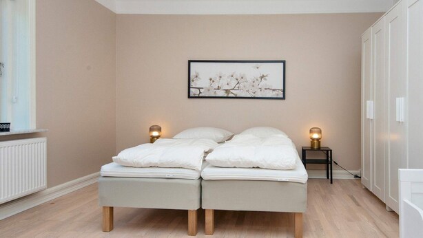 Una camera da letto con un letto, lampade sui comodini, un termosifone e un quadro appeso al muro.