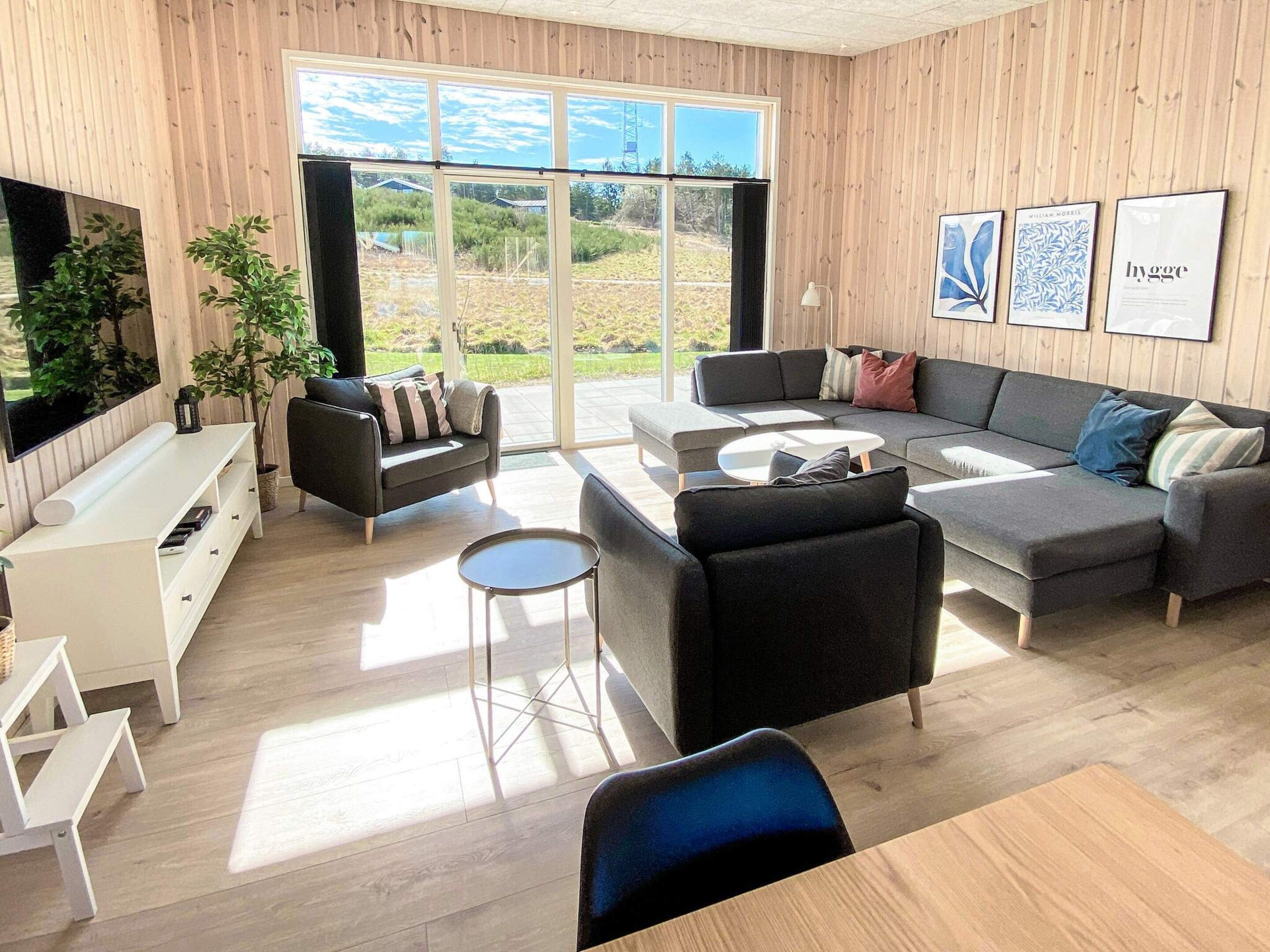 Un salon moderne avec un grand canapé, une table basse et un téléviseur. Des plantes et des œuvres d’art décorent les murs.