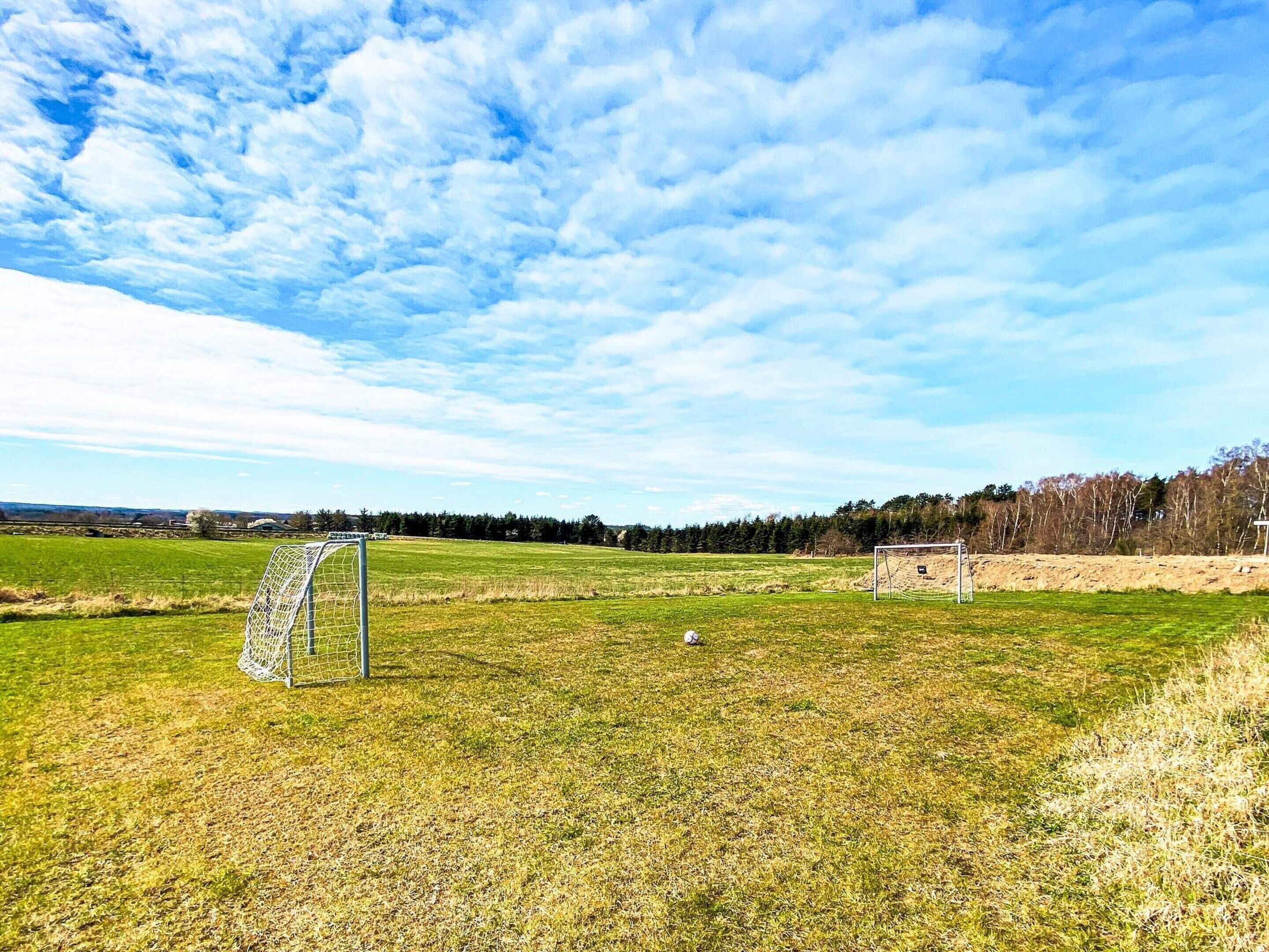 A soccer field with two goals, a clear sky, and a distant forest.