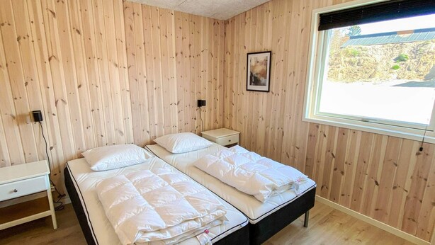 Een kamer met twee bedden, een nachtkastje, een klein tafeltje en een raam met uitzicht op de omgeving.