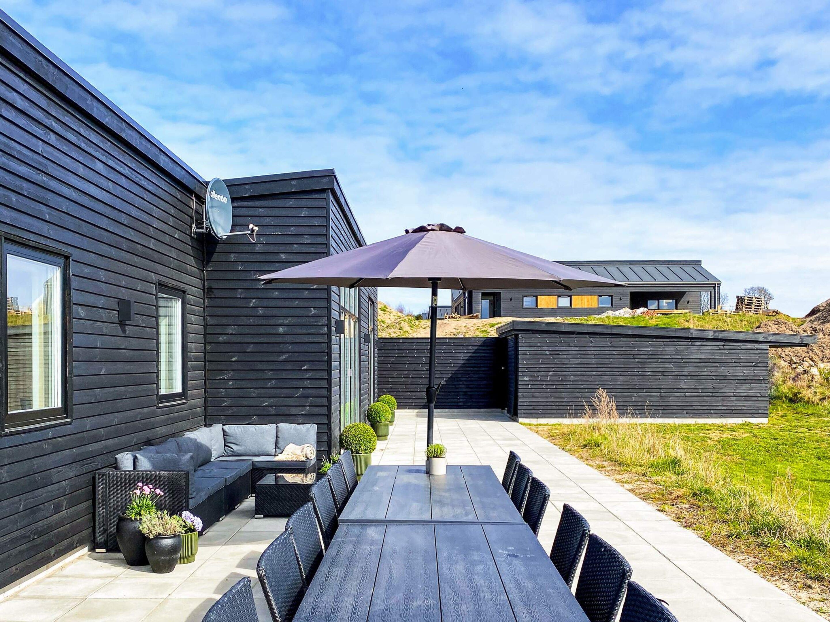 A modern outdoor patio with a dining table, chairs, and a large umbrella.