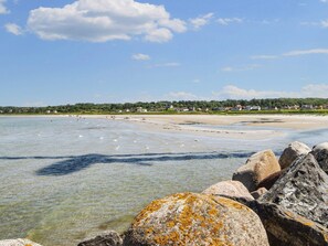Un paisaje costero con aguas claras, una playa de arena y una fila de casas al fondo.
