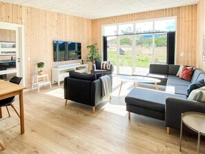 Una sala de estar moderna con detalles de madera, un televisor de pantalla plana, un sofá, una mesa de centro y un comedor.