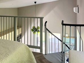 A bedroom with a bed, a window with a view of a body of water, a staircase with a railing, and a ceiling light. - 4 Star Holiday Home in Ljungby (Ljungby)