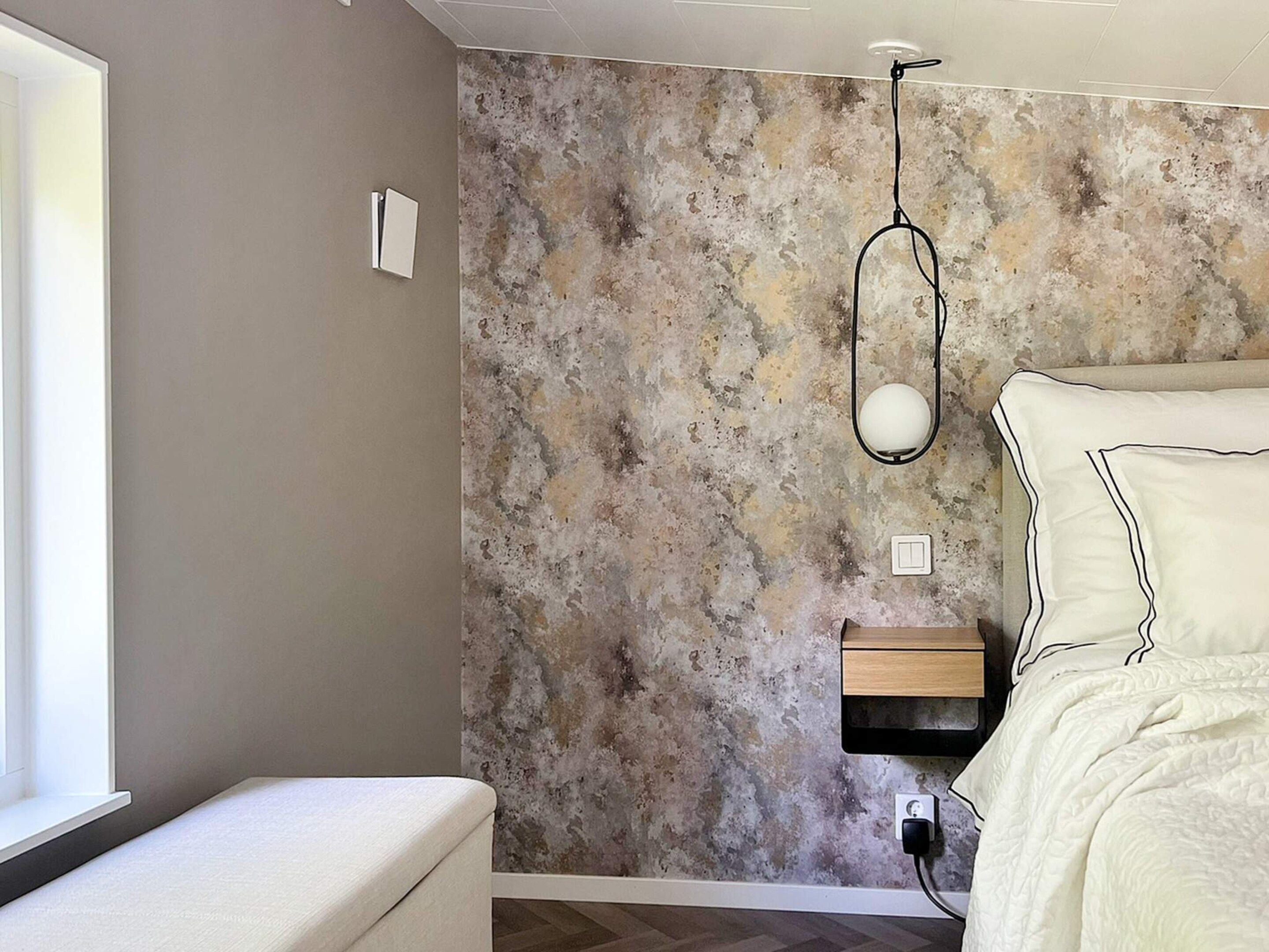 A bedroom with a bed, bedside table, and a wall with a textured pattern.