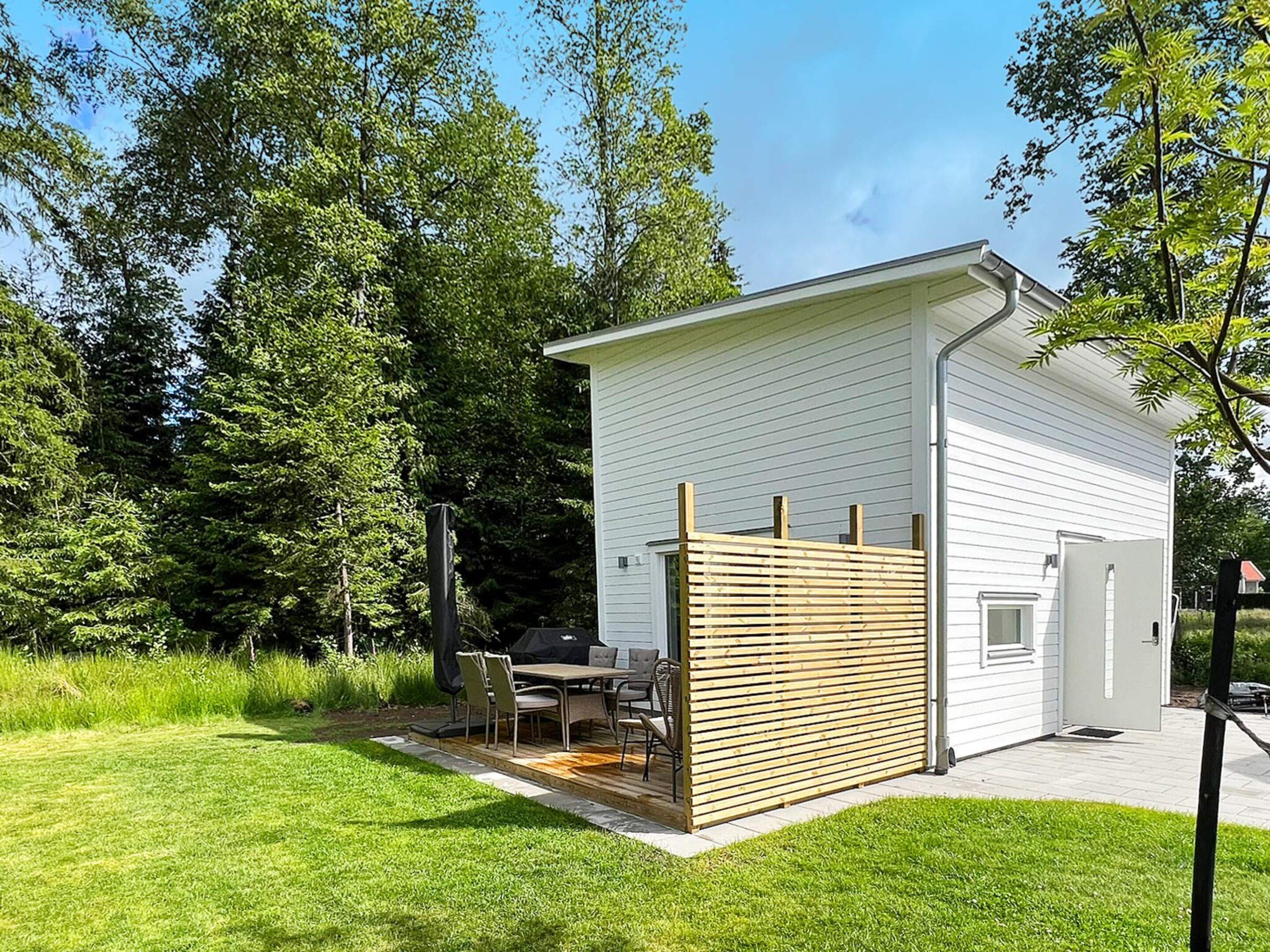 A small, single-story building with a flat roof, a wooden fence, and a patio area with outdoor furniture.