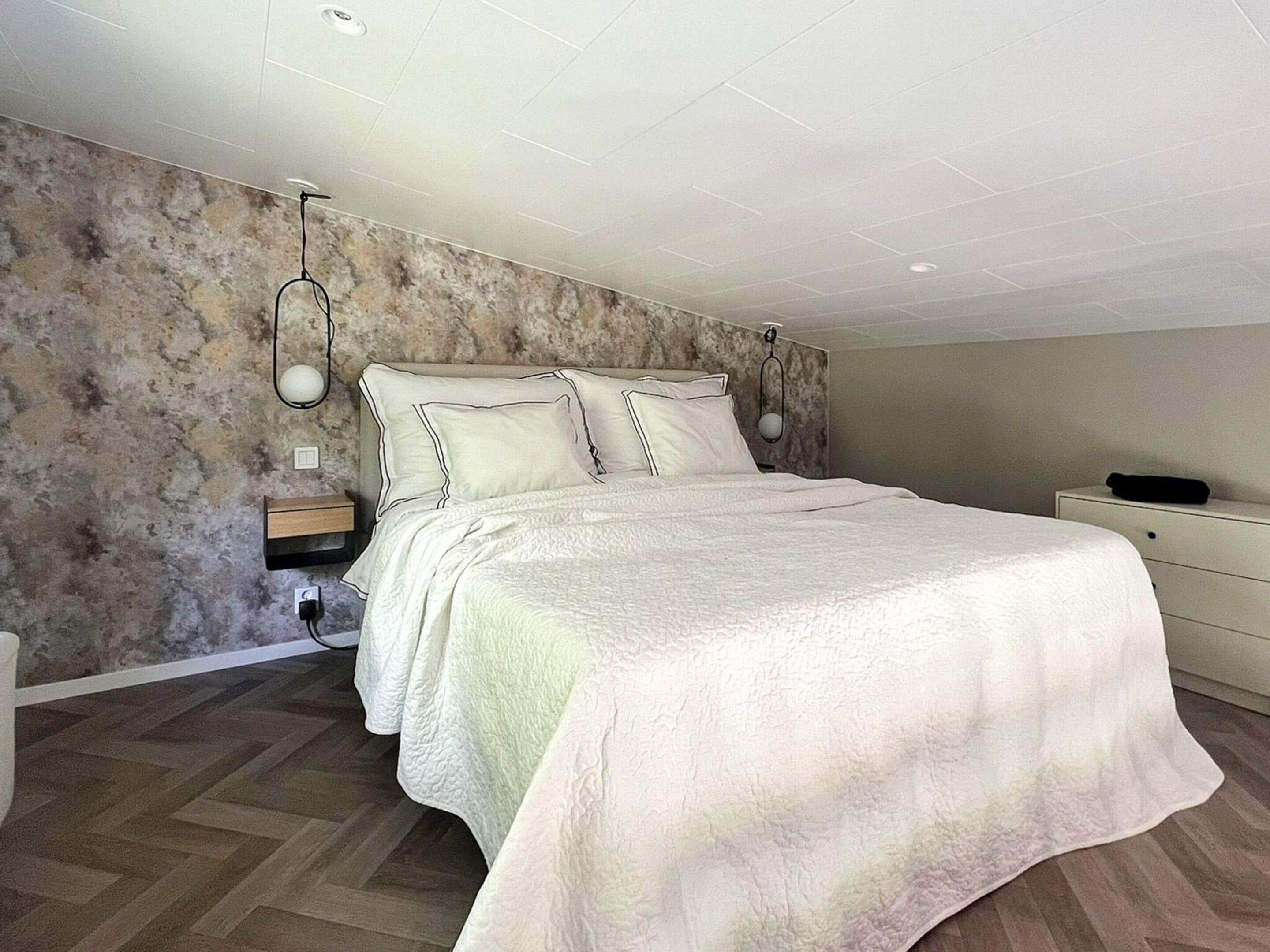 A bedroom with a bed, nightstands, a dresser, and a textured wall.