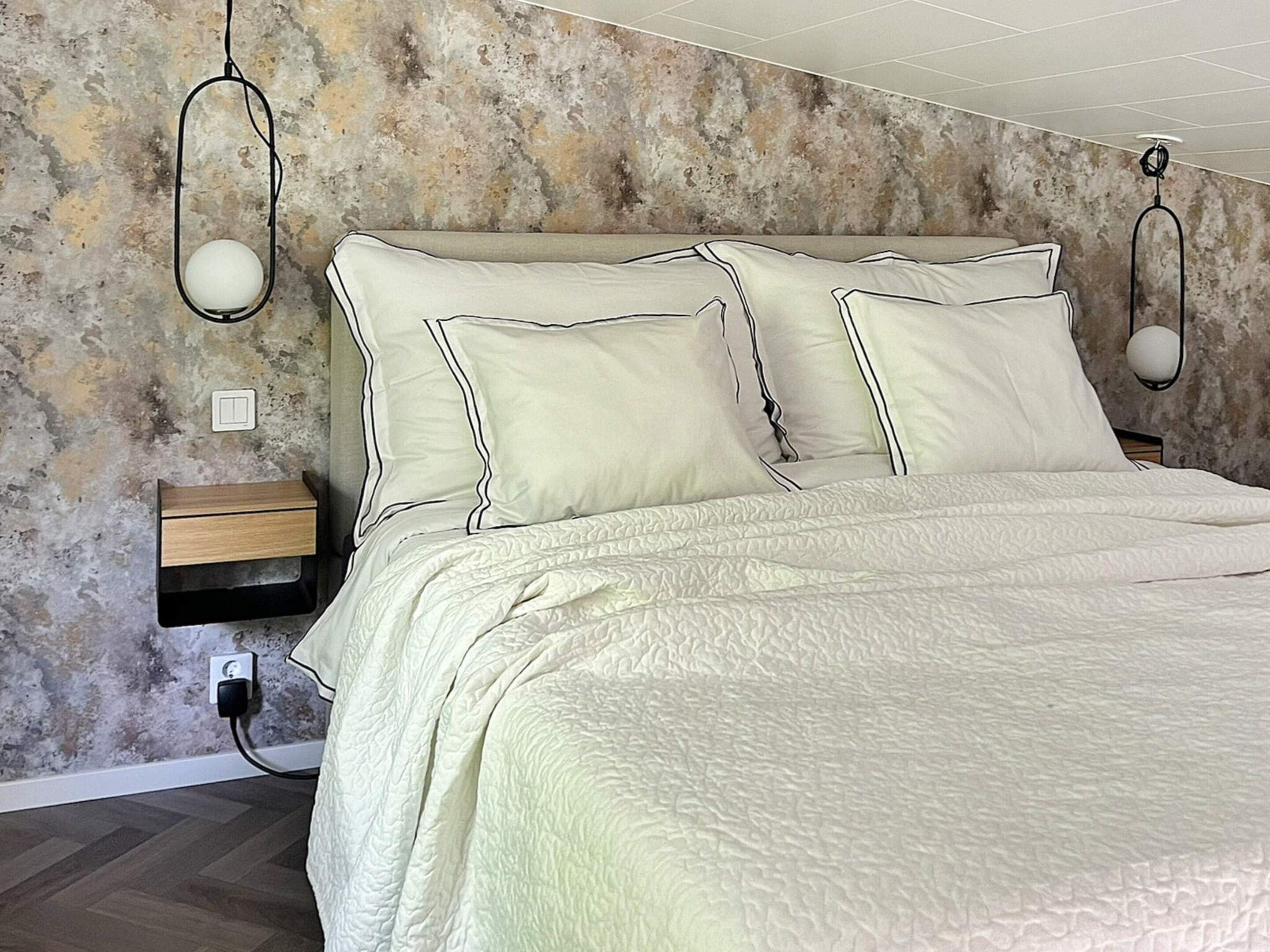 A bedroom with a bed, bedside tables, and wall-mounted lamps.