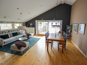 A spacious living room with a high ceiling, a dining area with a wooden table and chairs, and a large window providing natural light. - 7 Person Holiday Home in Mellbystrand (Mellbystrand)