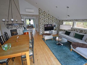 A modern living room with a wooden dining table, a grey sofa, and a TV. - 7 Person Holiday Home in Mellbystrand (Mellbystrand)