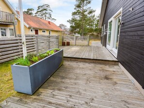 A wooden deck with a planter box containing plants, a wooden fence, and a building with a dark exterior and a window. - 7 Person Holiday Home in Mellbystrand (Mellbystrand)
