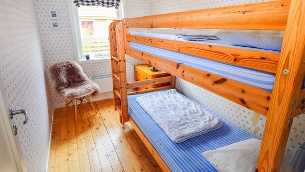 A bunk bed with a wooden frame and blue bedding, a small chair, and a window with a checkered curtain. - 7 Person Holiday Home in Mellbystrand (Mellbystrand)