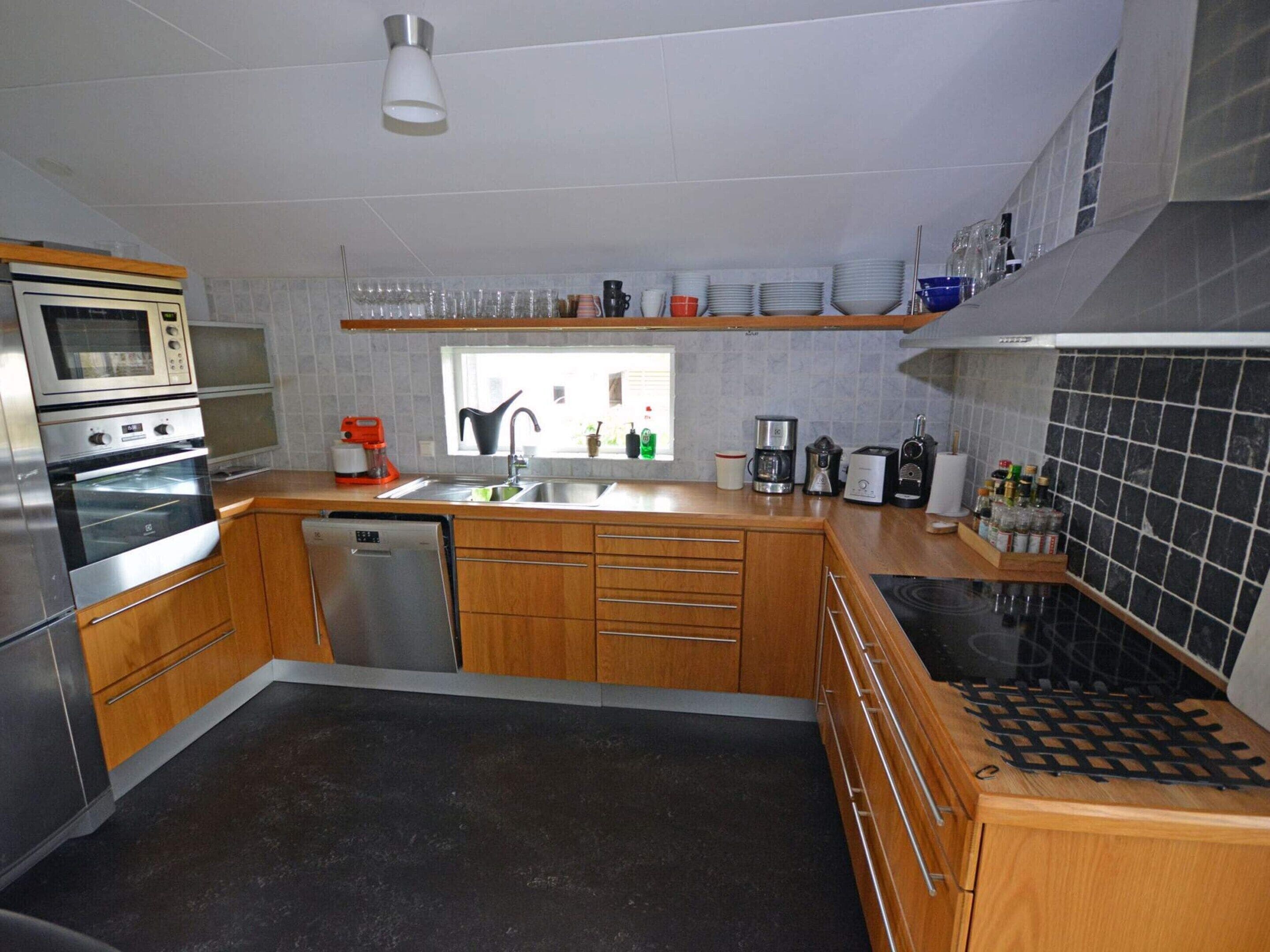 A modern kitchen with stainless steel appliances, wooden cabinets, and a black tiled backsplash.