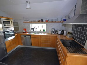 A modern kitchen with stainless steel appliances, wooden cabinets, and a black tiled backsplash. - 7 Person Holiday Home in Mellbystrand (Mellbystrand)