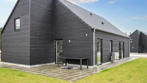 Ein modernes Gebäude mit geneigtem Dach, großen Fenstern und einer gepflasterten Terrasse.