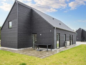 A modern building with a sloped roof, large windows, and a paved patio area. - 5 Star Holiday Home in Romo (Rømø)