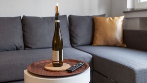 A bottle of wine on a round wooden table with a remote control beside it, placed in front of a grey sofa with a brown cushion. - Modern Apartment Fully and High Quality (Heilbronn)