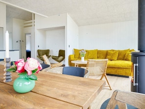 A modern living room with a wooden table, a yellow sofa, and wicker chairs. - 5 Star Holiday Home in Ronne (Ronne)