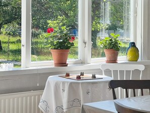 A room with a table set for dining, a window with potted plants, and a view of greenery outside. - 5 Star Holiday Home in Urshult (Urshult)