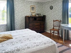 A bedroom with a bed, dresser, chair, and a window with curtains.