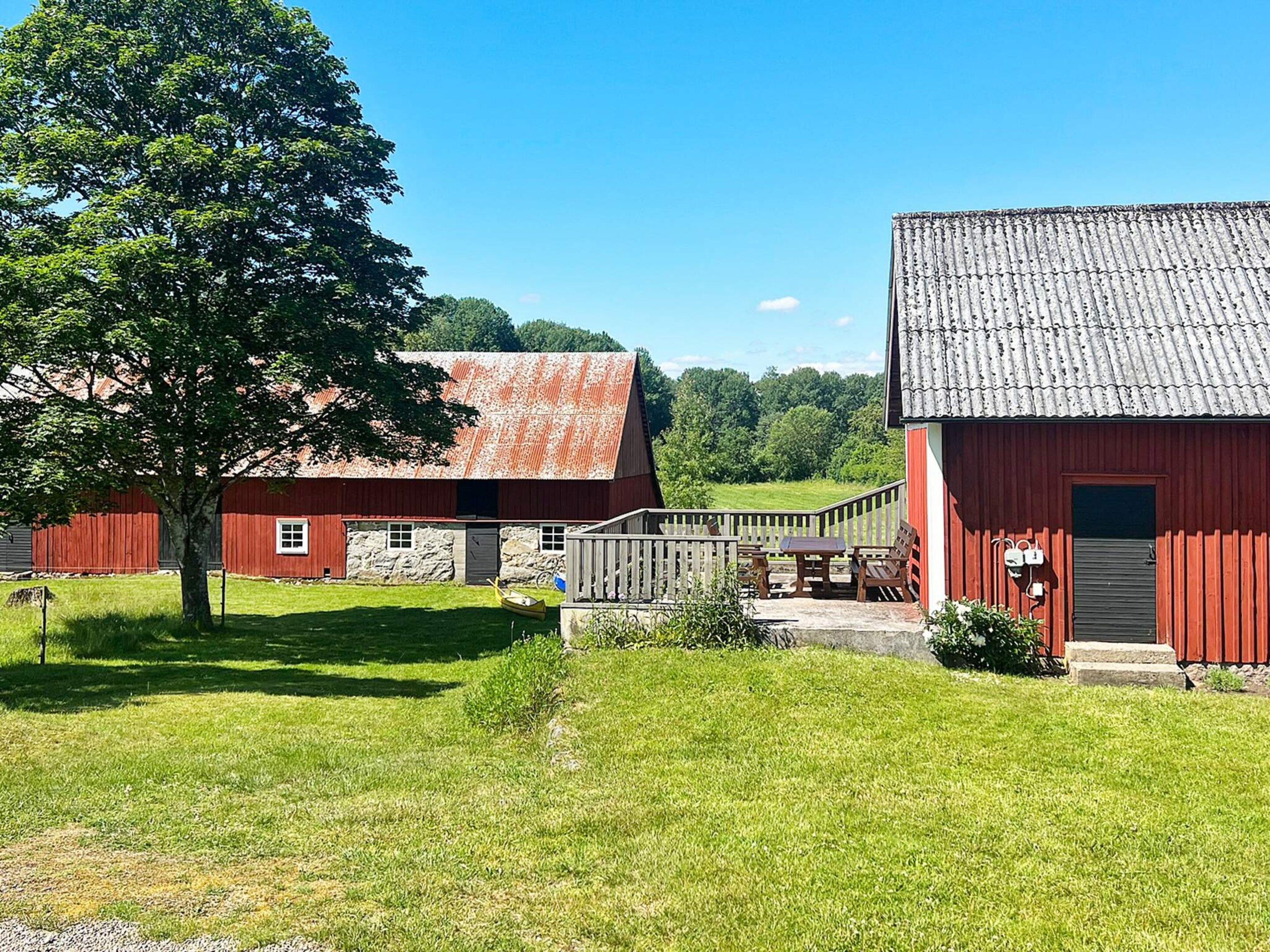 A red barn with a stone wall, a grassy yard, and a tree.