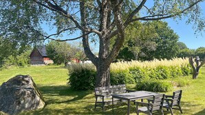 A picnic table with benches in a grassy area with trees and a red building in the background. - 5 Star Holiday Home in Urshult (Urshult)