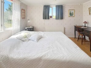 Un dormitorio con cama, escritorio, silla, ventana con cortinas y radiador.