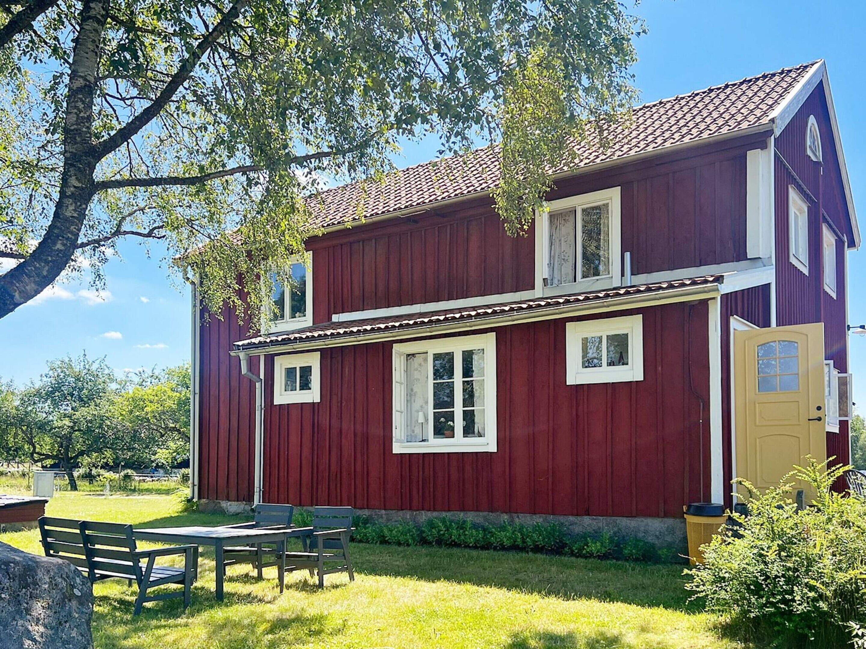 A red wooden house with a porch, a table, and chairs outside.
