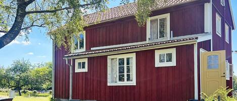 A red wooden house with a porch, a table, and chairs outside.
