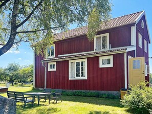 Et rødt træhus med en veranda, et bord og stole udenfor.