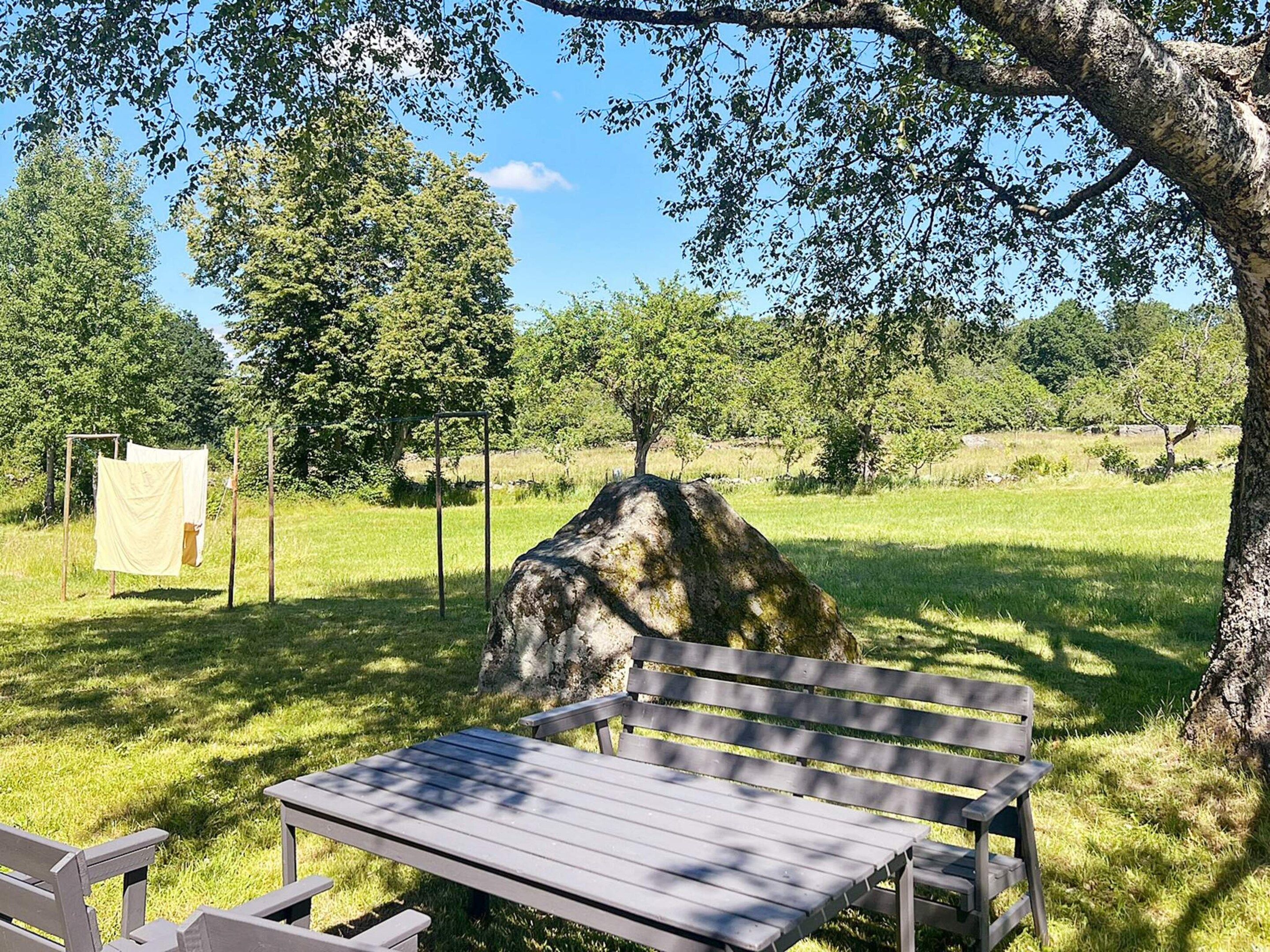 Un banco de parque bajo un árbol, una mesa de picnic y un letrero al fondo.