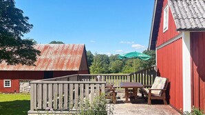 A red barn with a wooden deck, picnic table, and benches. - 5 Star Holiday Home in Urshult (Urshult)