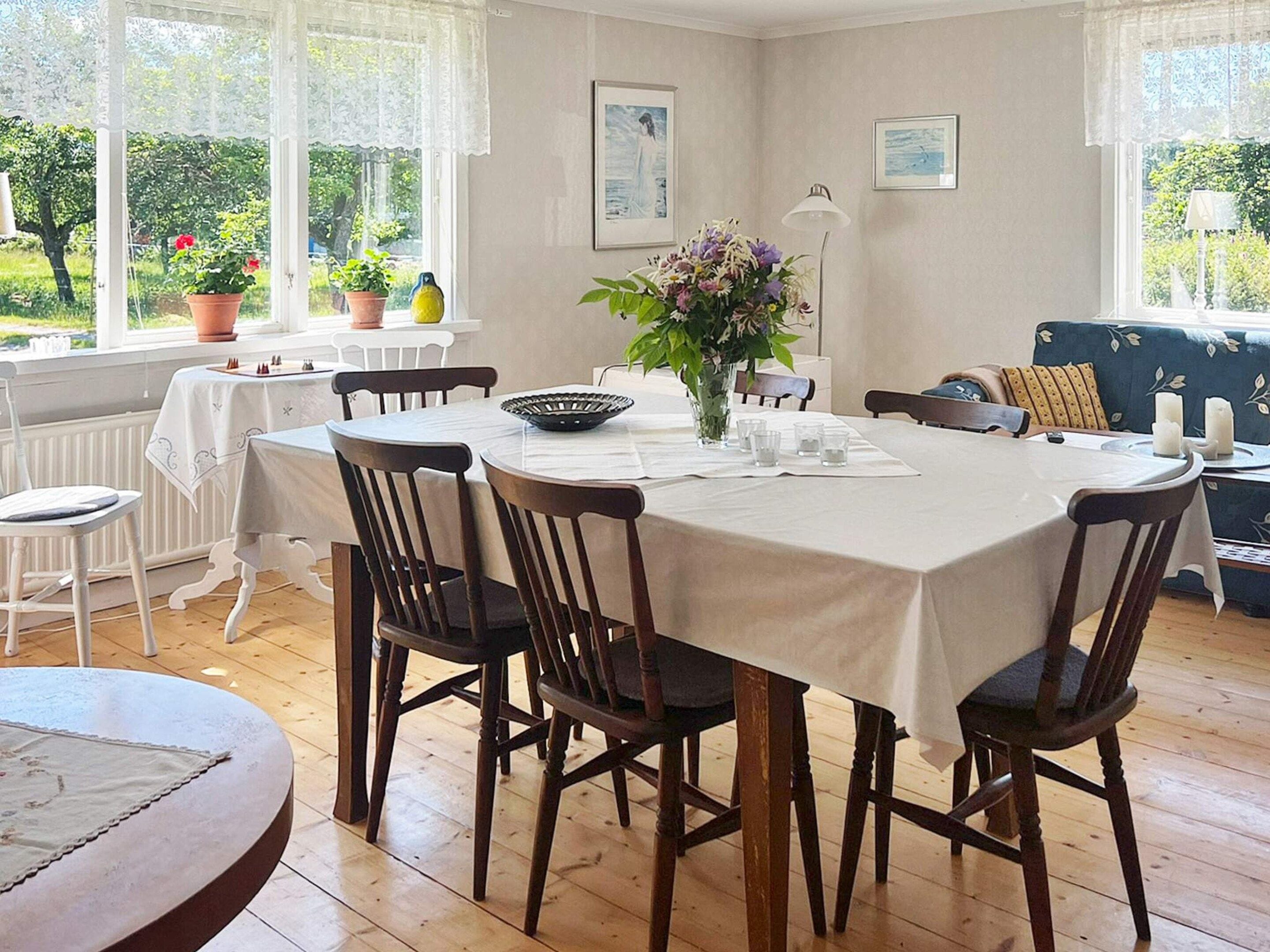 Uma sala de jantar com uma mesa redonda, cadeiras, um vaso com flores e um sofá.