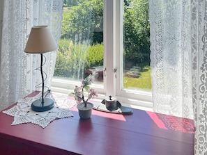 A window with lace curtains, a table with a lamp, a small potted plant, and a decorative item. - 5 Star Holiday Home in Urshult (Urshult)