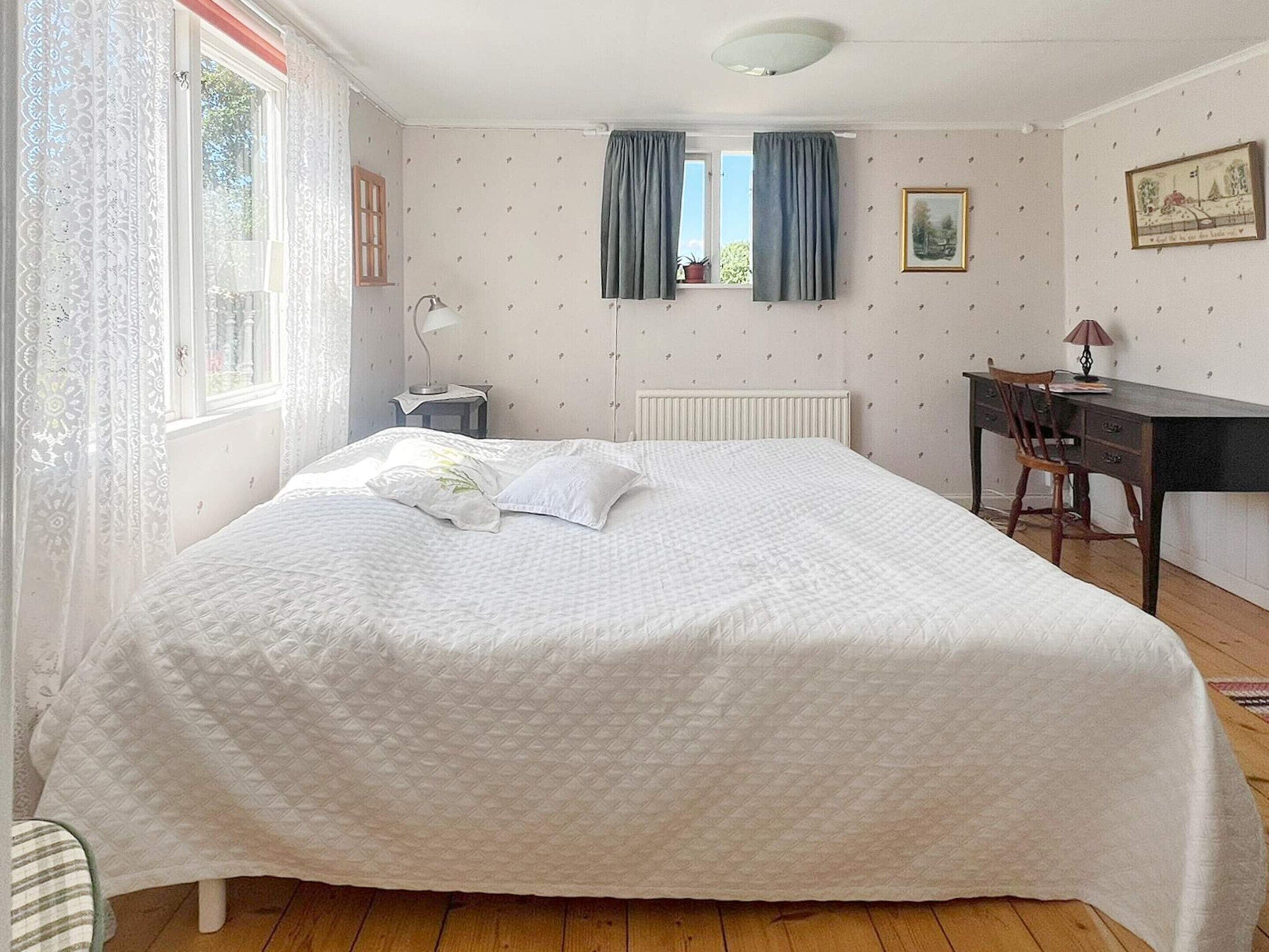 A bedroom with a bed, a desk, a chair, a radiator, and a window with curtains.