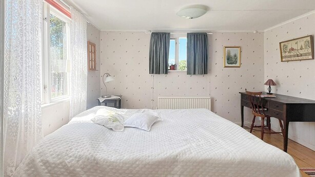 A bedroom with a bed, a desk, a chair, a radiator, and a window with curtains. - 5 Star Holiday Home in Urshult (Urshult)