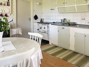 A kitchen with white cabinets, a stove, and a sink. There is a table with a white tablecloth and a chair.