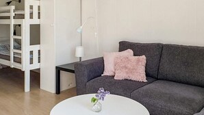 A living room with a grey sofa, a white coffee table with a vase of flowers, a white lamp, and a white bunk bed in the background. - 4 Star Holiday Home in Karlskrona (Karlskrona)