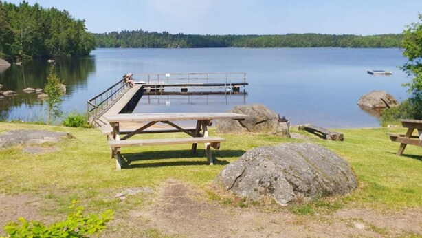 A lakeside picnic area with a wooden deck, picnic tables, and a dock extending into the water. - 4 Star Holiday Home in Karlskrona (Karlskrona)